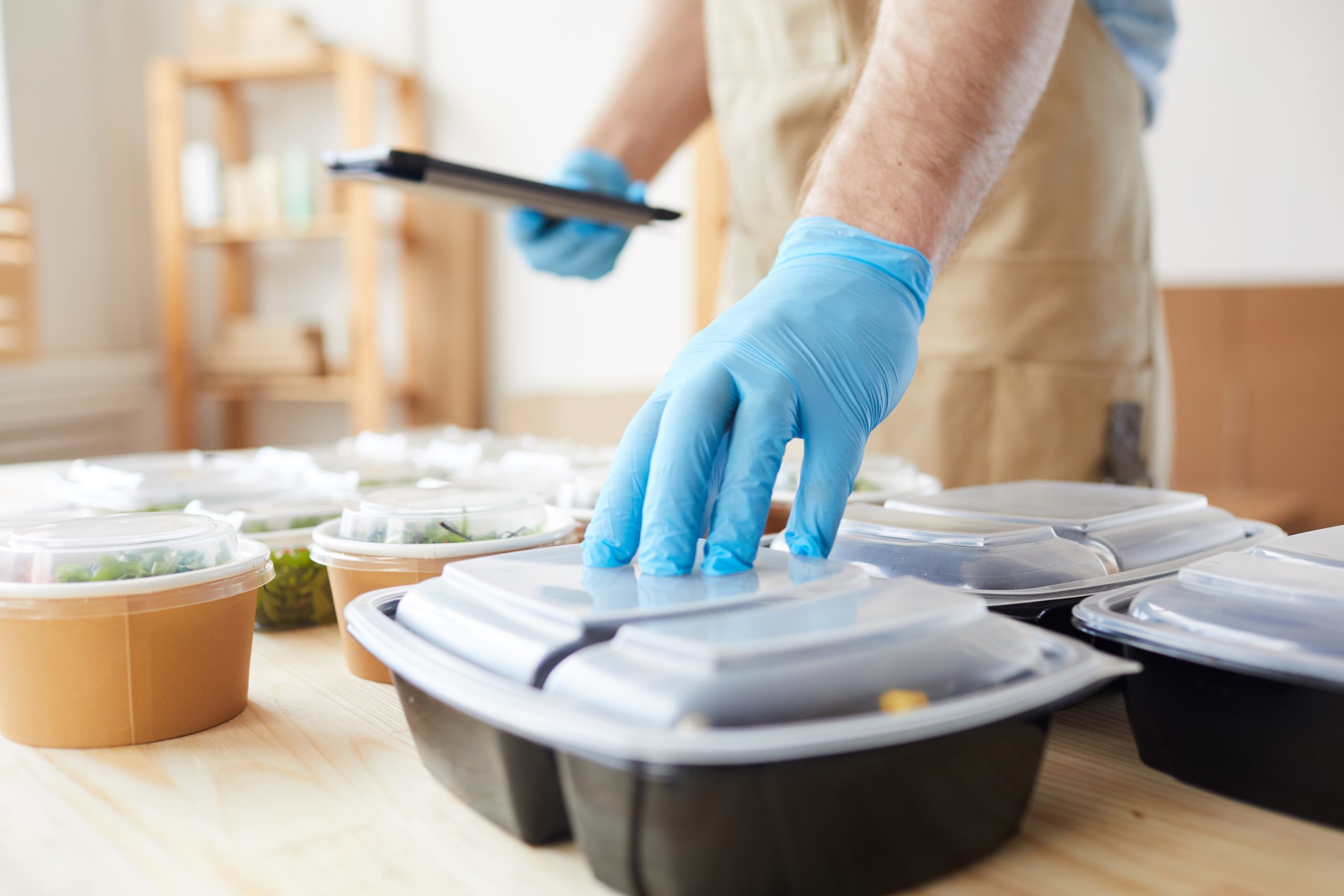 Close-up of delivery person in protective gloves preparing food in boxes for delivery