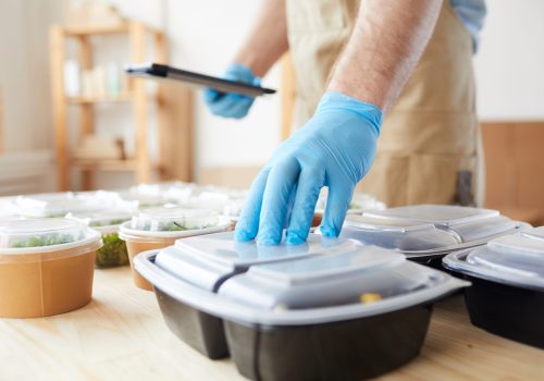 Close-up of delivery person in protective gloves preparing food in boxes for delivery