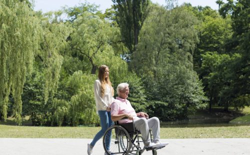 Young girl walking in the park with elder man on a wheelchair